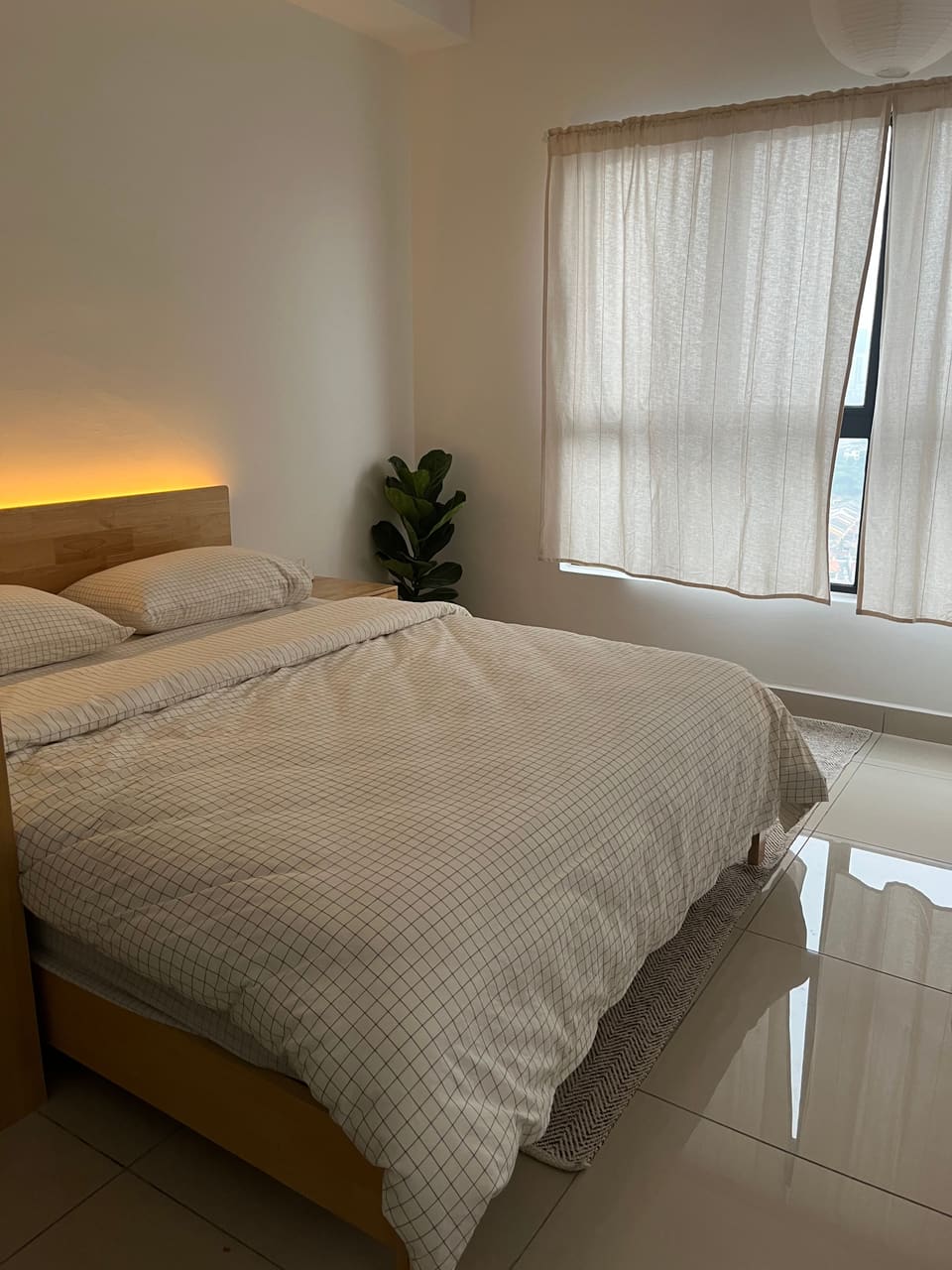 Queen bed with checked linen, soft headboard light and a plant