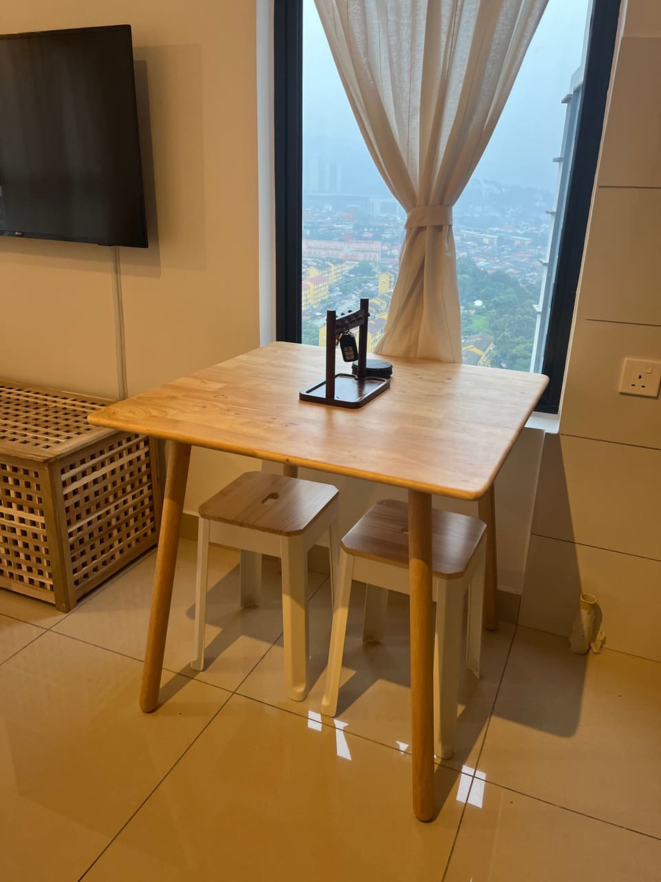 Wooden table for two beside a tall window with a city view