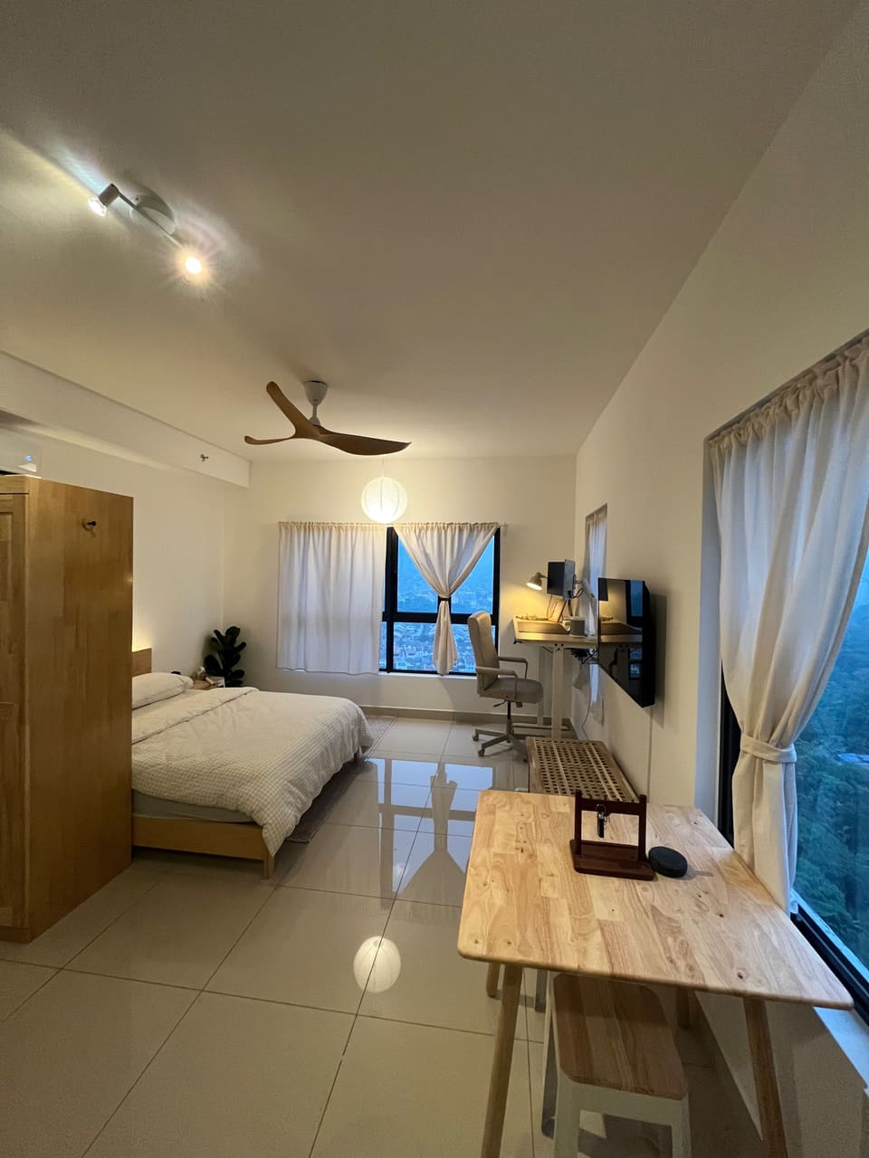 The whole studio at dusk: queen bed, desk corner and wooden dining table